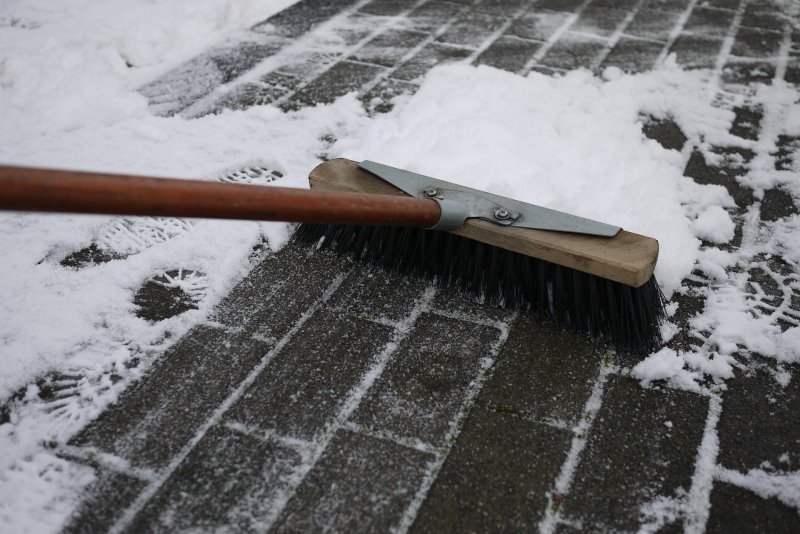 Ein Stahlbesen fegt den Schnee von einem Fußweg.